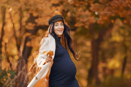 Pregnant woman in a brown coat in a autumn parkの写真素材