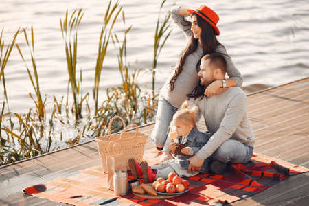 Family with little daughter sitting near water in a autumn parkの写真素材