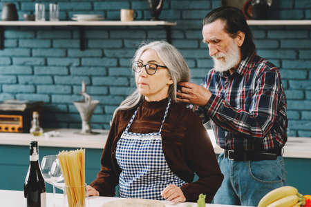 Senior couple putting on aprons before preparing food in kitchenの写真素材