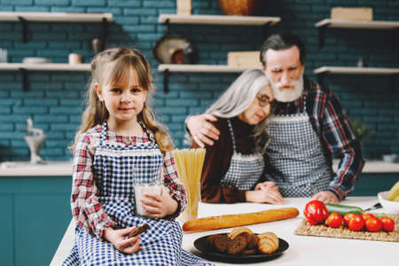 Little girl eating in the kitchen with granparentsの写真素材