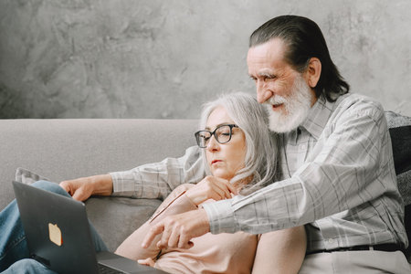 Senior couple sitting on couch with laptopの写真素材