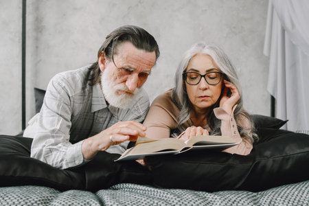 Senior couple reading book lying together on bed