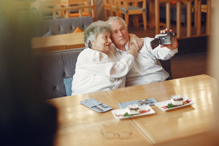 Elegant old couple in a cafe using a camera
