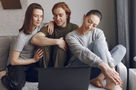 Friends sitting on a bed in a room and use a laptop