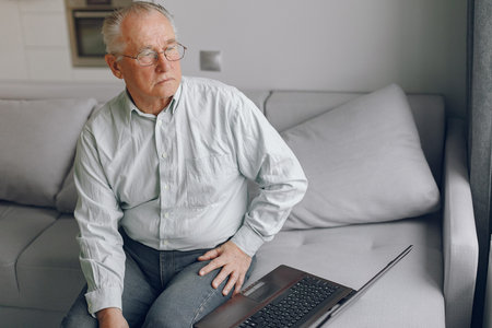 Elegant old man sitting at home and using a laptop