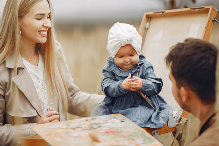 Family with little daughter painting in a autumn field
