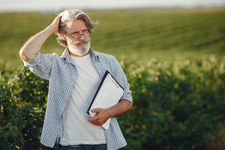 Old farmer in shirt standing on field with notebookの写真素材
