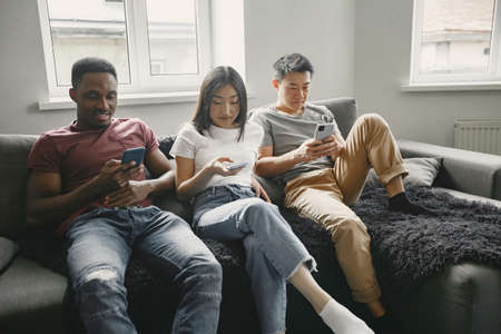 Three friends sitting on the sofa in the living room and staring at the phoneの写真素材