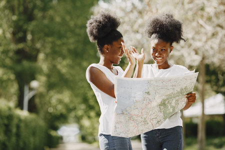 Young african-american twin sisters looking in a map near park