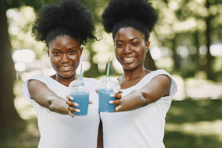 Twin sisters holding a cups with drinks and looking in a cameraの写真素材