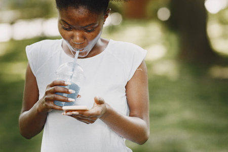 Portrait of a smiling young african-american girl holding a blue drink in a park