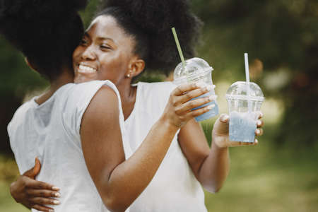 Two young afro-american sisters hugging in a parkの写真素材