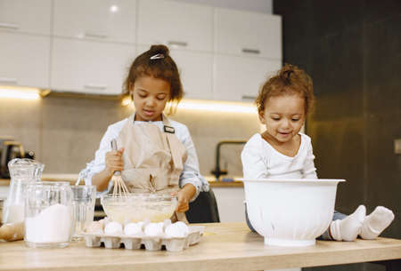 Two children in a kitchen. Little girls with a dough. Kid in a beige apronの写真素材