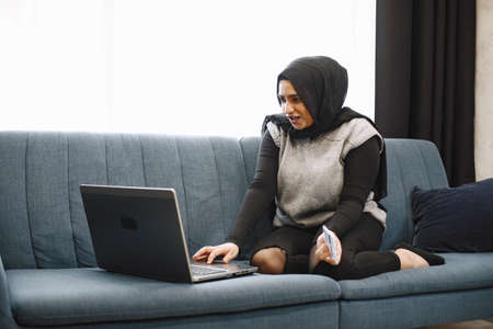 Arabic woman in headscarf using laptop at home, paying for utilities online.の写真素材