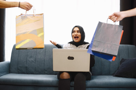 Arabic woman in headscarf using laptop at home, doing shopping online