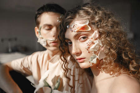 Emotional portrait of a boy and girl with flowers on their faceの写真素材