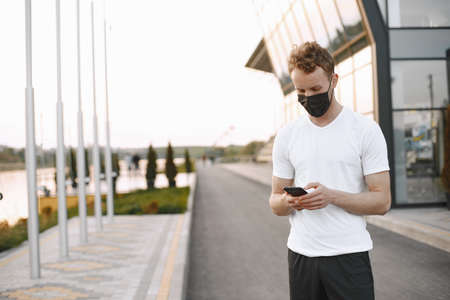 Portrait of a young fit man in a face mask jogging outdoors on a stadiumの写真素材