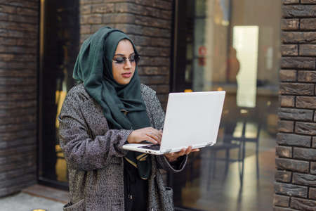 Portrait of a muslim girl in a green hijab with a laptop on the streetの写真素材