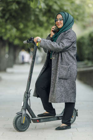 Portrait of a muslim girl in a green hijab with a scooter on the streetの写真素材