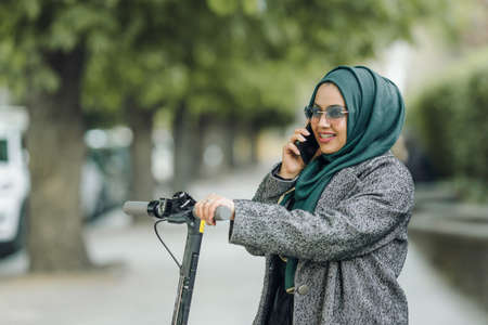 Portrait of a muslim girl in a green hijab with a scooter on the streetの写真素材