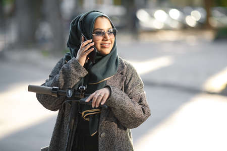 Portrait of a muslim girl in a green hijab with a scooter on the streetの写真素材