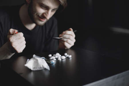Addict preparing drug dose for injection in dark roomの写真素材