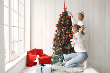 Mother with little daughter sitting by the Christmas tree and having fun.の写真素材