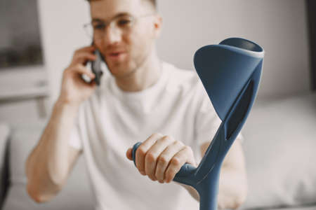 Young man with walking stick talk by phone indoorsの写真素材