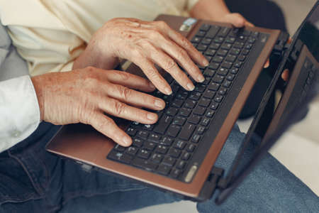 Elegant old couple sitting at home and using a laptopの写真素材