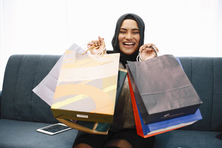 Arabic woman in headscarf sitting on a sofa with packages. Girl did online shoppingの写真素材