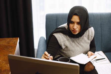 Arabic woman in headscarf using laptop at home, paying for utilities online.の写真素材