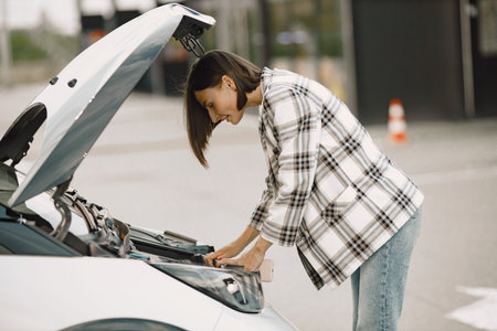 Portrait of a young brunette woman looking in a car hood on an engine