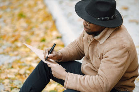 Black man sitting on a road and writing a sign for autostopの写真素材