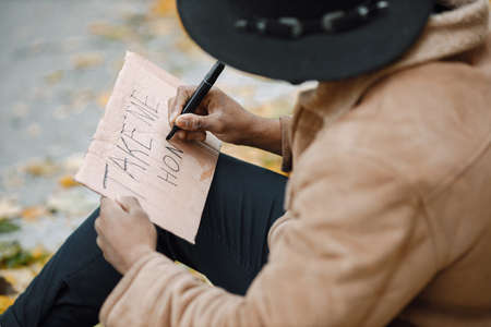 Black man sitting on a road and writing a sign for autostopの写真素材