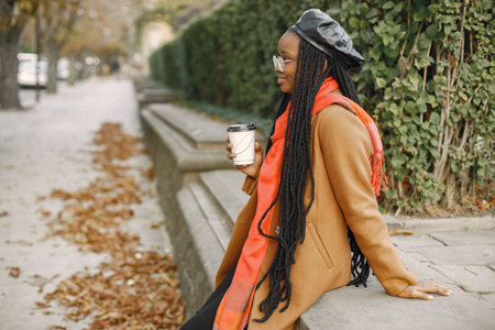 Young black woman in a coat drinking coffee outside