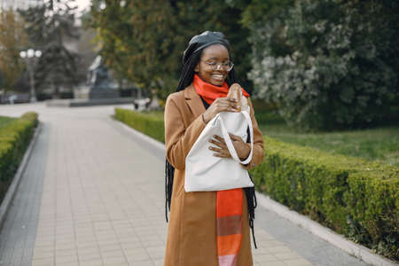 Young black woman in a coat standing outside holding a bag with a breadの写真素材