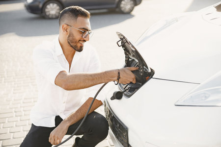 Young Arab man recharging white electric car