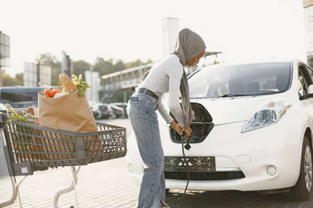 African American girl charging electro car at the electric gas stationの写真素材