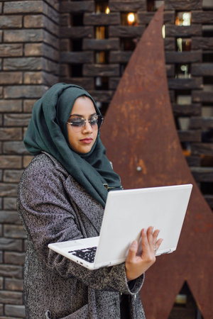 Portrait of a muslim girl in a green hijab with a laptop on the street