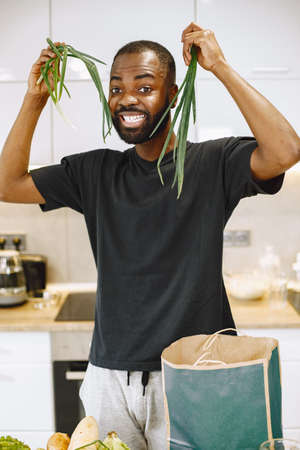 African-american man in a kitchen holding a green onionの写真素材