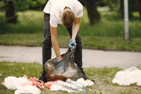 Boy volunteer picks up a trash in a parkの写真素材