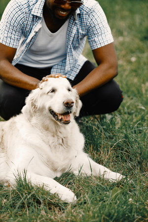 Black american man in a sunglasses sitting with has dog on a grassの写真素材