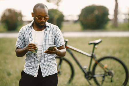 Black american man in a sunglasses standing on a grass and using a phoneの写真素材