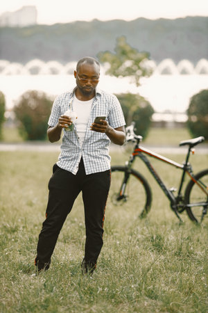 Black american man in a sunglasses standing on a grass and using a phone