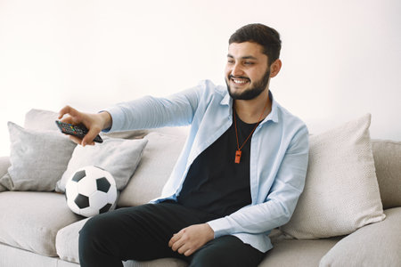 Brunette guy sitting on a coach and watching football at homeの写真素材
