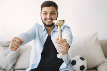 Brunette guy sitting on a coach and watching football at homeの写真素材
