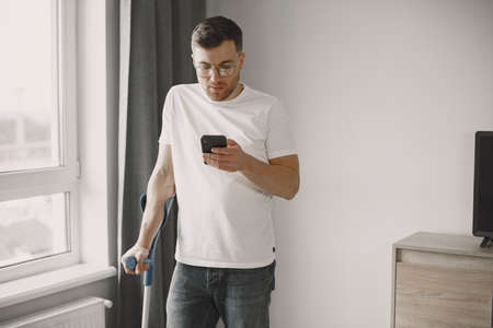 Young man with walking stick talk by phone indoorsの写真素材