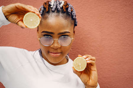 Black girl standing on a wall backgroung with a lemonsの写真素材