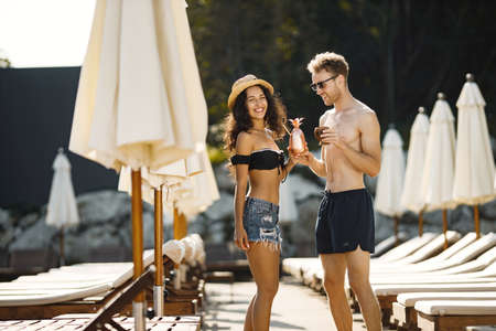 Portrait of a young girl and her boyfriend with a cocktails standing near sunbedsの写真素材