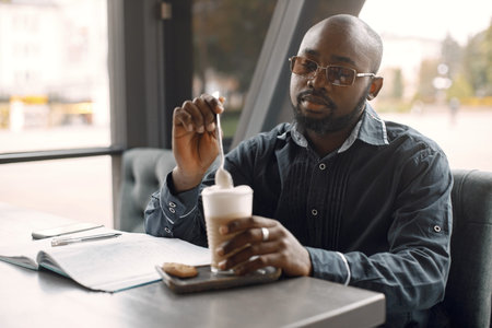 Black man sitting in a cafe with a cup of latte and papersの写真素材